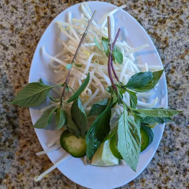 A plate of herbs used to top beef noodle soup