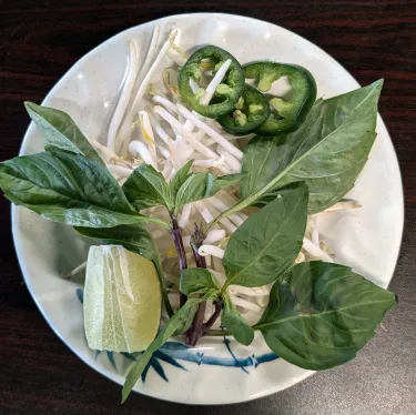 A plate of herbs used to top beef noodle soup