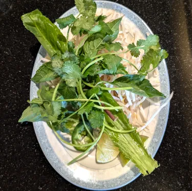 A plate of herbs used to top beef noodle soup