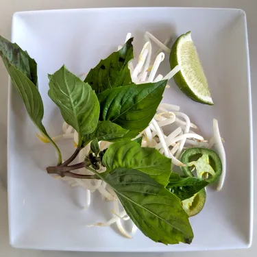 A plate of herbs used to top beef noodle soup