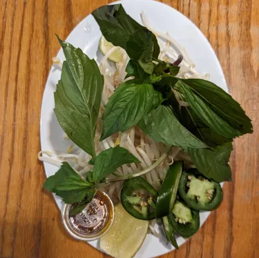 A plate of herbs used to top beef noodle soup