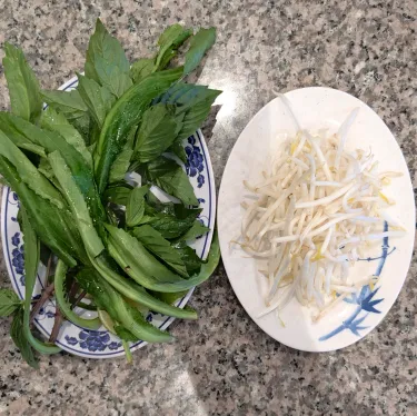 A plate of herbs used to top beef noodle soup