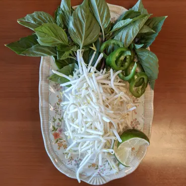 A plate of herbs used to top beef noodle soup