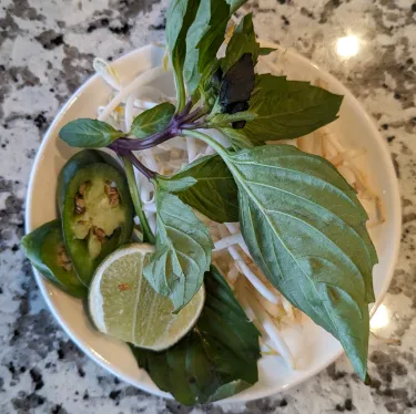 A plate of herbs used to top beef noodle soup