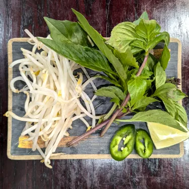 A plate of herbs used to top beef noodle soup